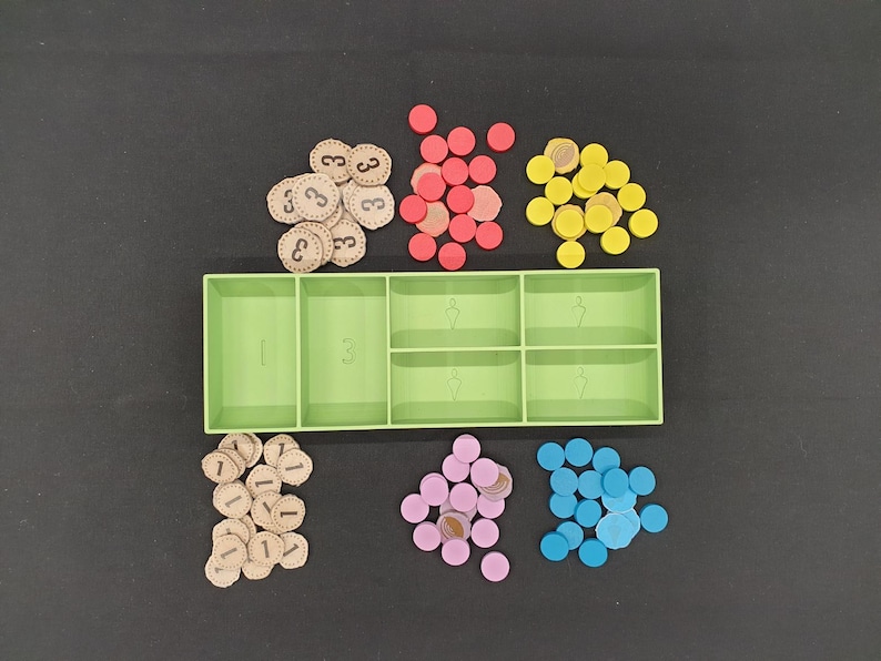 May include: A green plastic organizer with six compartments, filled with various game pieces. There are beige tokens with the number "3" printed on them, red, yellow, pink, and blue circular tokens, and beige tokens with the number "1" printed on them.