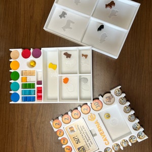 May include: White plastic organizer with compartments for game pieces. The organizer has a white base and a clear top. The compartments are labeled with numbers and symbols. The organizer is for the board game Caverna: The Cave Farmers.