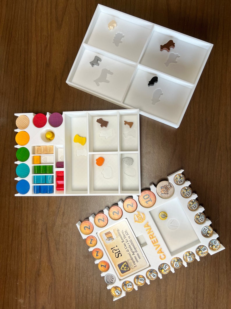 May include: White plastic organizer with compartments for game pieces. The organizer has a white base and a clear top. The compartments are labeled with numbers and symbols. The organizer is for the board game Caverna: The Cave Farmers.