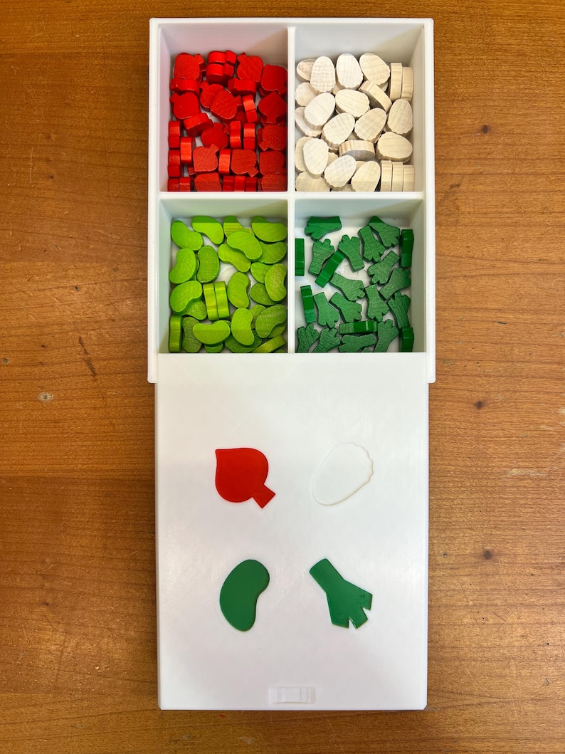 May include: A white plastic tray with four compartments filled with wooden game pieces. The compartments contain red, white, green, and green pieces. The tray also has a smaller compartment with four sample pieces: a red heart, a white circle, a green bean, and a green broccoli.