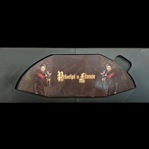 K&ouml;nnte beinhalten: Eine schwarze Box mit einem Scharnierdeckel, ge&ouml;ffnet, um ein Spielbrett mit zwei Figuren in historischen Kost&uuml;men zu zeigen. Das Spielbrett tr&auml;gt den Titel "Principi di Firenze".