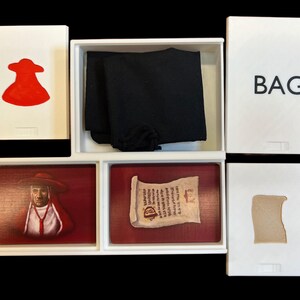 May include: A white box with a red figure, a black cloth, a scroll, a portrait of a man in a red robe, and a brown piece of paper. The box is labeled "BAG".