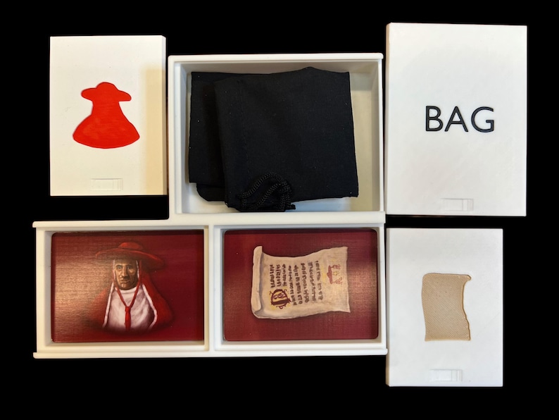 May include: A white box with a red figure, a black cloth, a scroll, a portrait of a man in a red robe, and a brown piece of paper. The box is labeled "BAG".