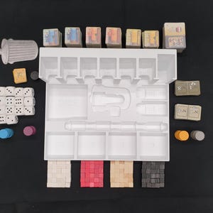 May include: A white plastic game organizer with various game pieces, including dice, tokens, and small cards. The organizer has multiple compartments and slots to hold the game components. The pieces are in various colors, including white, red, and gray.
