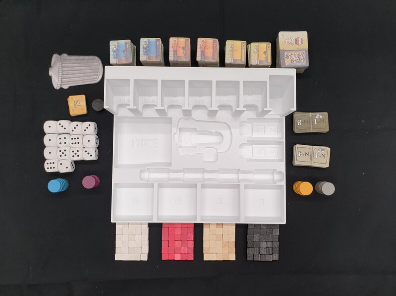 May include: A white plastic game organizer with various game pieces, including dice, tokens, and small cards. The organizer has multiple compartments and slots to hold the game components. The pieces are in various colors, including white, red, and gray.