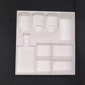 Puede incluir: Un organizador de juego de pl&aacute;stico blanco para el juego de mesa Stone Age: The Expansion. El organizador tiene varios compartimentos de diferentes formas y tama&ntilde;os, incluyendo espacios para piezas y cartas del juego. El texto "Stone Age: The Expansion" es visible.