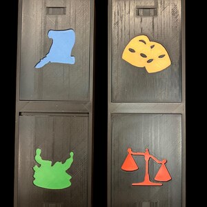 May include: Two wooden boxes with different colored shapes cut out. The top box on the left has a light blue hat shape, the bottom box has a green monster shape. The top box on the right has a yellow mask shape, the bottom box has a red scale shape.