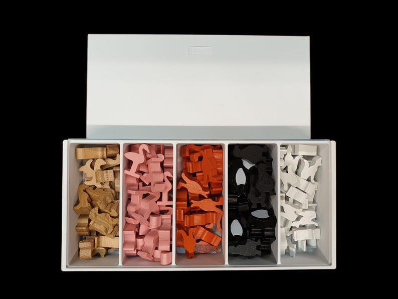 May include: A white plastic storage box with five compartments, each filled with small wooden animal figurines. The compartments contain pink, orange, black, and white figurines.