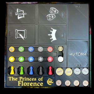 Op de afbeelding: Een zwarte spelorganizer met vakken voor spelstukken, dobbelstenen en geld. De organizer heeft de tekst "The Princes of Florence" op de voorkant.