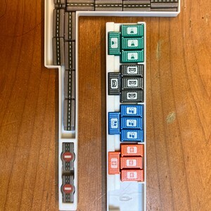 Pode incluir: Uma bandeja de pl&aacute;stico branco com uma pista cinza e uma variedade de recipientes coloridos. Os recipientes s&atilde;o empilhados em filas e s&atilde;o etiquetados com diferentes s&iacute;mbolos. A bandeja &eacute; projetada para um jogo de tabuleiro.