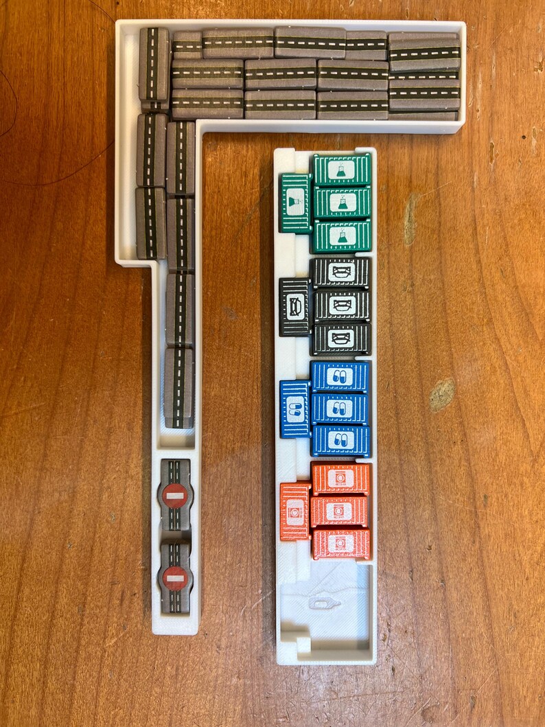 Pode incluir: Uma bandeja de pl&aacute;stico branco com uma pista cinza e uma variedade de recipientes coloridos. Os recipientes s&atilde;o empilhados em filas e s&atilde;o etiquetados com diferentes s&iacute;mbolos. A bandeja &eacute; projetada para um jogo de tabuleiro.