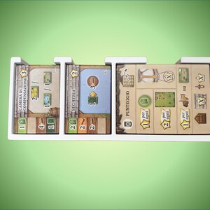 May include: A white organizer with five compartments for storing game cards. The cards are labeled "Camera di Compensazione", "Segheria", "Punteggio", and have numbers and symbols on them.