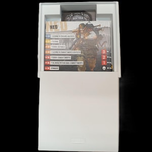May include: A white box containing game cards with Italian text and a card featuring a character illustration. The cards have action descriptions and numerical values. A small card with the word "POLICE" is visible.