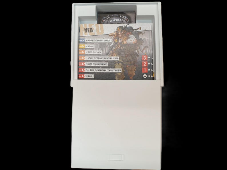May include: A white box containing game cards with Italian text and a card featuring a character illustration. The cards have action descriptions and numerical values. A small card with the word "POLICE" is visible.