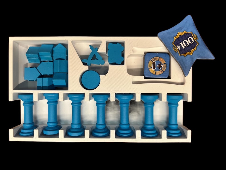 May include: A white foam insert with blue plastic game pieces. The insert has compartments for storing different shapes and sizes of pieces. There are also seven blue columns. A blue dice with a +1 symbol and a blue pillow with the text +100 are also included.
