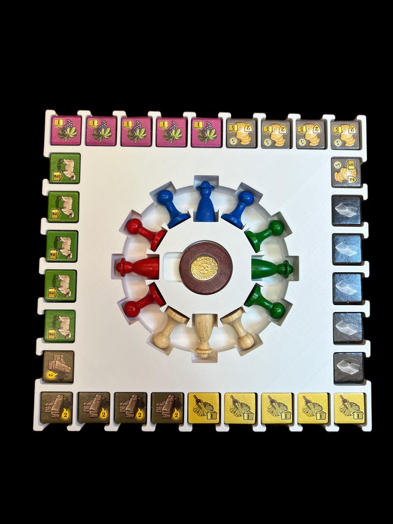 May include: A white game board with a central circular area containing a wooden spinning wheel with colored pegs. The board has a grid of squares with various colored tiles depicting different resources. The tiles are labeled with numbers.