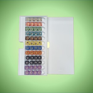 May include: A white plastic storage case with a clear lid containing a collection of colorful round beads. The beads are arranged in rows and are different colors, including red, orange, yellow, green, blue, purple, and black.