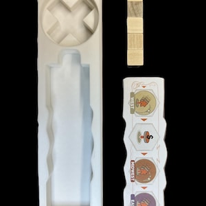 May include: A white foam insert with a cross-shaped cutout and a long rectangular slot. There are four wooden blocks stacked on top of each other. A white card with the words "East", "Midwest", and "West" and illustrations of a maple leaf, a spinning top, and a beehive.