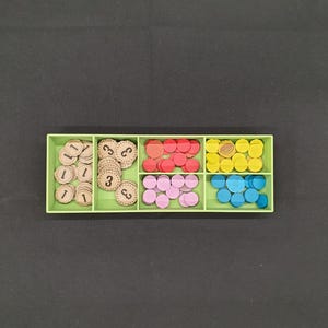 May include: A light green organizer filled with game pieces. The pieces are various colors, including red, pink, yellow, and blue. Some pieces are wooden discs with the numbers 1 and 3 printed on them.