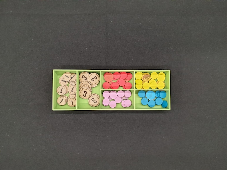 May include: A light green organizer filled with game pieces. The pieces are various colors, including red, pink, yellow, and blue. Some pieces are wooden discs with the numbers 1 and 3 printed on them.