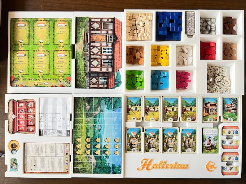 May include: A white organizer with compartments for storing game pieces and cards. The organizer has a white background with a brown and white house illustration. The organizer is labeled "Hallertau".