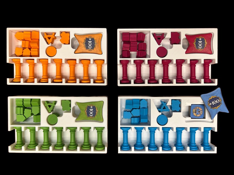 May include: Four white trays with different coloured game pieces and cards. Each tray has 10 columns with small pillars in each column. The trays have a card with the text " +100" in the top right corner. The colours of the game pieces are orange, red, green, and blue.