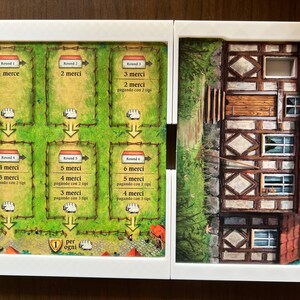 May include: A game board with six rounds of play, each with a different number of sheep and a corresponding number of "merci" points. The board is made of cardboard and has a green background with brown fences. The board is divided into six sections, each with a different number of sheep. The board also has a small house on the right side.