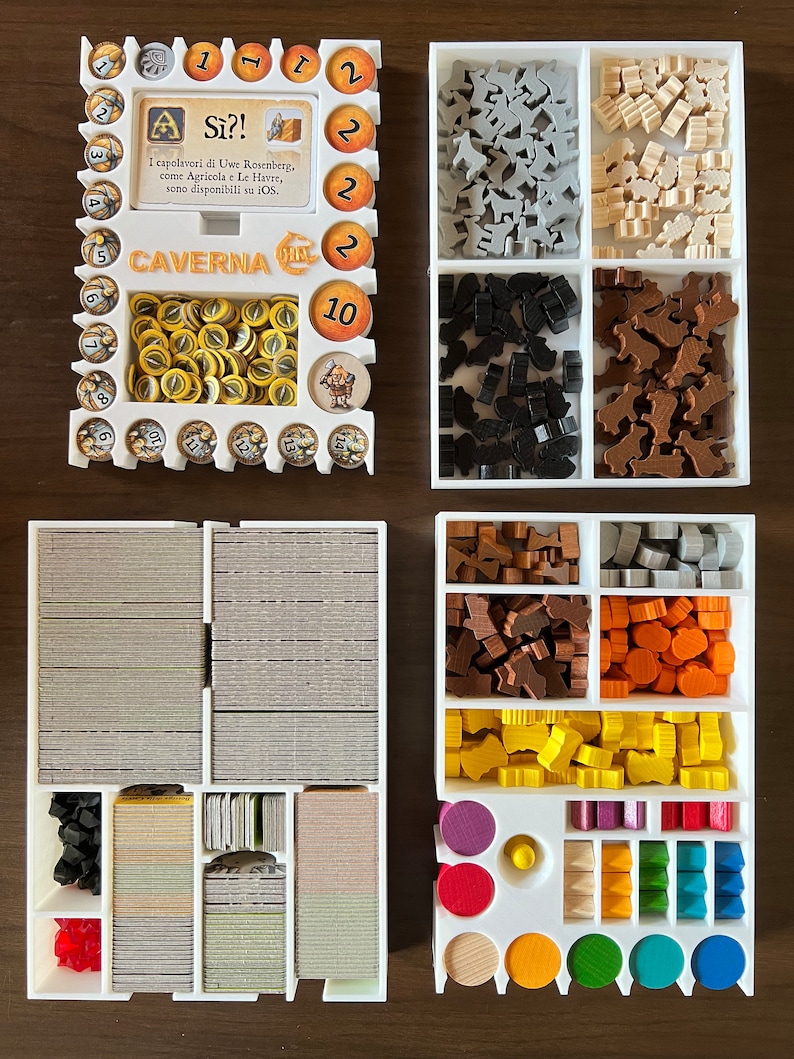 May include: White plastic organizer with multiple compartments for storing game pieces. The organizer has a label that reads "Caverna" and "S&igrave;?!". The game pieces are in various colors, including brown, black, gray, white, yellow, orange, red, and green.