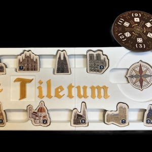 May include: A white game board with the word "Tiletum" printed in gold letters. The board has nine slots for game pieces, each with a number from 1 to 9. There are also two additional slots for a compass and a die. The game pieces are small, detailed images of buildings.