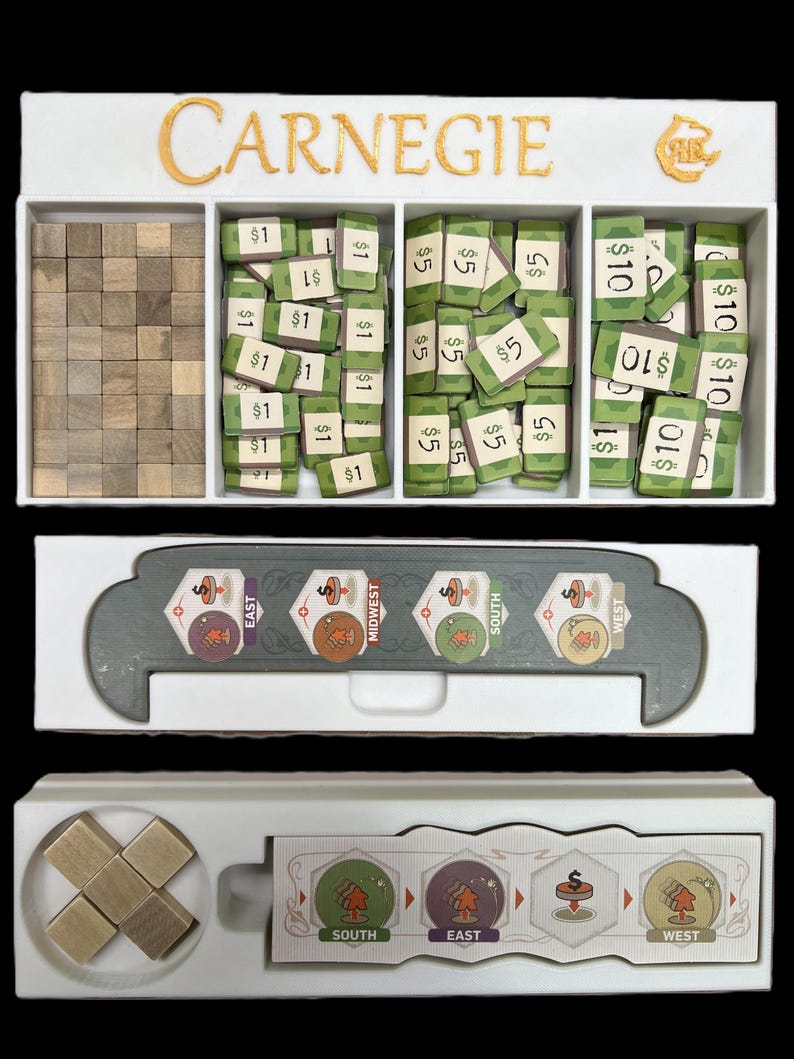 May include: A white wooden game organizer with the word "CARNEGIE" printed in gold letters. The organizer has three compartments, one for wooden cubes, one for dollar bills, and one for $5 and $10 bills. The organizer also has a compartment for game cards.