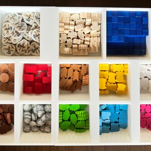 May include: A white tray with 10 compartments, each containing a different color of wooden game pieces. The pieces are arranged in a grid pattern. The colors include brown, red, orange, yellow, white, green, blue, and pink.