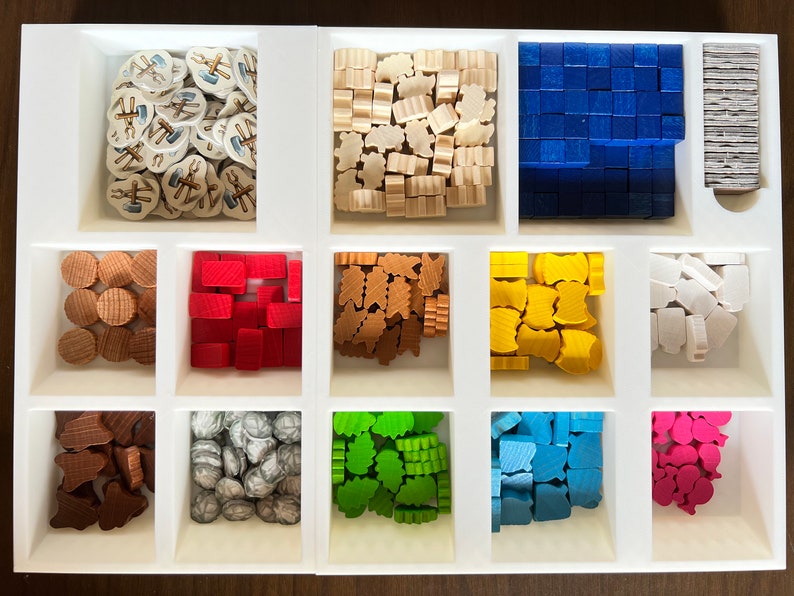 May include: A white tray with 10 compartments, each containing a different color of wooden game pieces. The pieces are arranged in a grid pattern. The colors include brown, red, orange, yellow, white, green, blue, and pink.