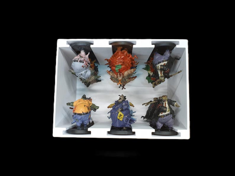 May include: A set of six detailed, colorful figurines of grotesque characters, each with unique designs and poses. The figures are arranged in a white display box against a black background, showcasing their intricate features and vibrant colors.