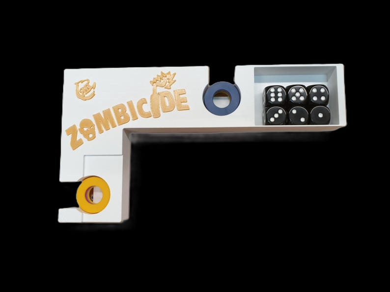 May include: A white wooden game organizer with the word "ZOMBICIDE" in gold lettering. The organizer has compartments for dice and other game components. Six black dice with white dots are visible.
