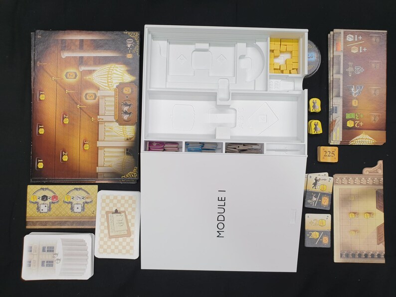 May include: A board game set with various components, including a game board, cards, and tokens. The game box is white with the text "MODULE I". The game board features a detailed illustration with warm colors.