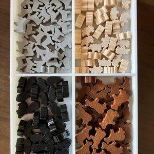 May include: A white tray with four compartments, each filled with wooden game pieces. The top left compartment contains gray animal-shaped pieces, the top right compartment contains light brown pieces, the bottom left compartment contains black pieces, and the bottom right compartment contains brown pieces.