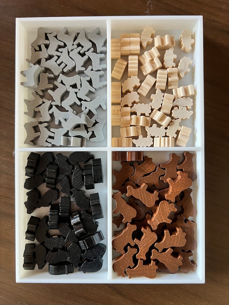 May include: A white tray with four compartments, each filled with wooden game pieces. The top left compartment contains gray animal-shaped pieces, the top right compartment contains light brown pieces, the bottom left compartment contains black pieces, and the bottom right compartment contains brown pieces.