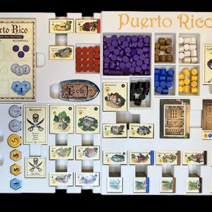 Może przedstawiać: Biała plansza do gry z tytułem "Puerto Rico" w złotych literach. Plansza jest podzielona na sekcje z r&oacute;żnymi elementami gry, w tym drewnianymi kostkami, żetonami i kartami. Plansza jest przeznaczona do gry planszowej.