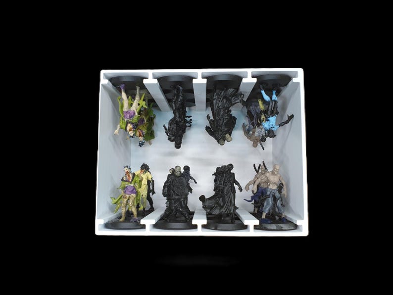 May include: A white tray holds eight miniature figurines. The figurines are of various characters, some in green, purple, and blue, others in black. The figures are on black bases.