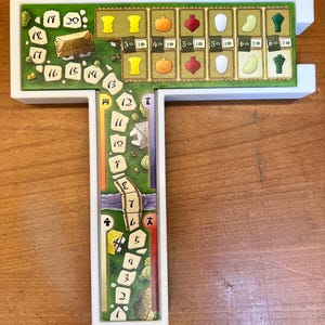 May include: A white plastic game board with a green and brown game piece track. The track has numbers 1 through 20. The board has a T-shape with a separate section at the top with a row of 6 different colored game pieces. The game pieces are yellow, orange, red, white, green, and blue.