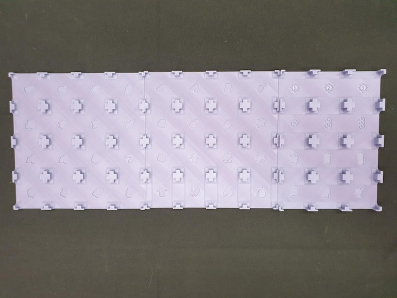 May include: A light purple interlocking tile set, made up of several rectangular pieces. Each tile features a grid of cross-shaped connectors and small, embossed shapes. The tiles are designed to interlock, forming a larger surface area.