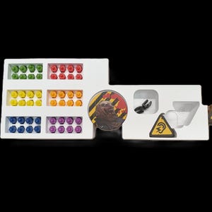 May include: A white game organizer with compartments holding colorful game pieces. Includes green, red, yellow, orange, blue, and purple pieces. Also features game tokens and a circular game piece with a graphic.