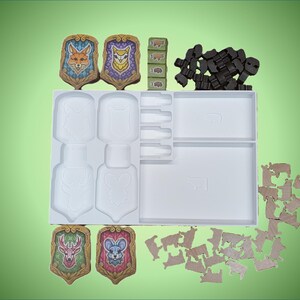 May include: A white plastic storage tray with compartments for game pieces. The tray contains four colorful shields with animal illustrations, a set of wooden cubes, and a collection of brown wooden pieces.