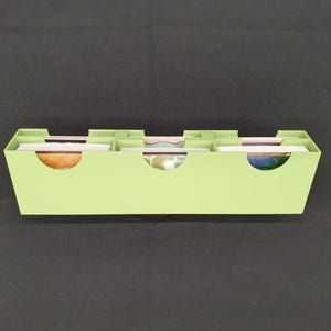 May include: A light green, rectangular card organizer with three curved cutouts. The organizer is divided into four sections, each holding a stack of colorful cards. The cards have various designs and colors.