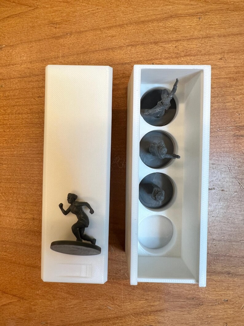 May include: A white rectangular container with a running figure figurine on a brown base. Next to it is a white container with three running figure figurines in circular compartments and a white sphere.