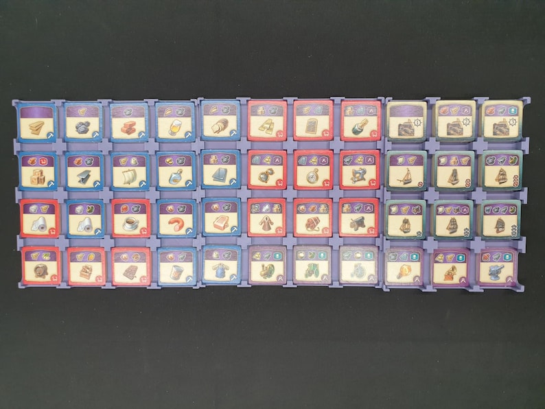 May include: A selection of game tiles arranged in rows. The tiles are square with various icons and colours, including blue, red, and purple. The icons depict items like food, tools, and resources. The tiles are set in a purple plastic frame.