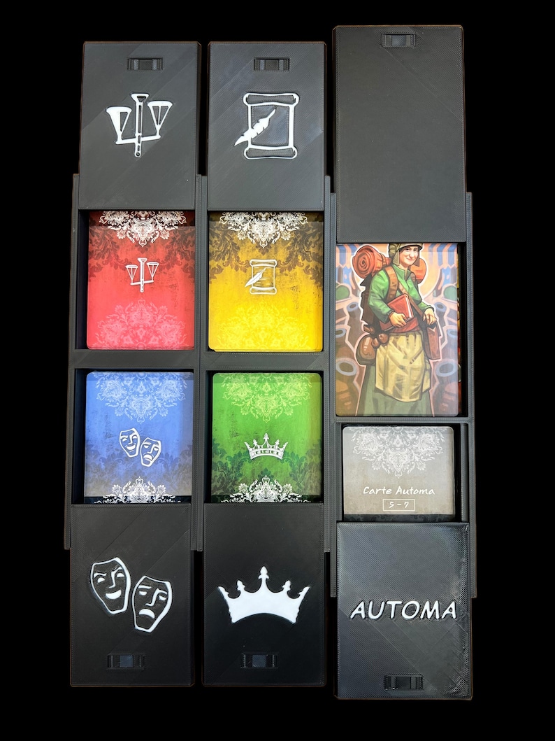 Pu&ograve; includere: Un organizzatore di giochi di carte nero con sei scomparti. Ogni scomparto ha un simbolo diverso sulla parte superiore, tra cui una bilancia, un rotolo, una corona e due maschere. La parte inferiore dell'organizzatore ha la parola "AUTOMA" stampata su di esso.