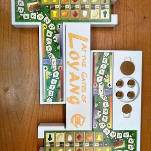 May include: A white plastic game board organizer for the board game "At the Gates of Loyang". The organizer has three sections, one for the game board, one for the player boards, and one for the game components. The organizer is designed to keep the game organized and easy to set up.