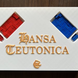 Może przedstawiać: Białe pudełko gry planszowej z tytułem "HANSA TEUTONICA" złotymi literami. Pudełko ma dwa przedziały, jeden z czerwonymi kostkami, a drugi z niebieskimi kostkami.