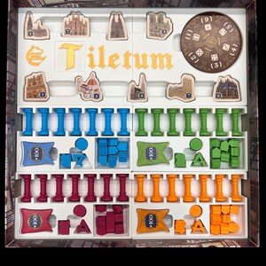 May include: A game box with the title "Tiletum" printed on the lid. The box contains various game pieces, including wooden tiles, plastic columns, and plastic cubes in blue, green, red, and orange.